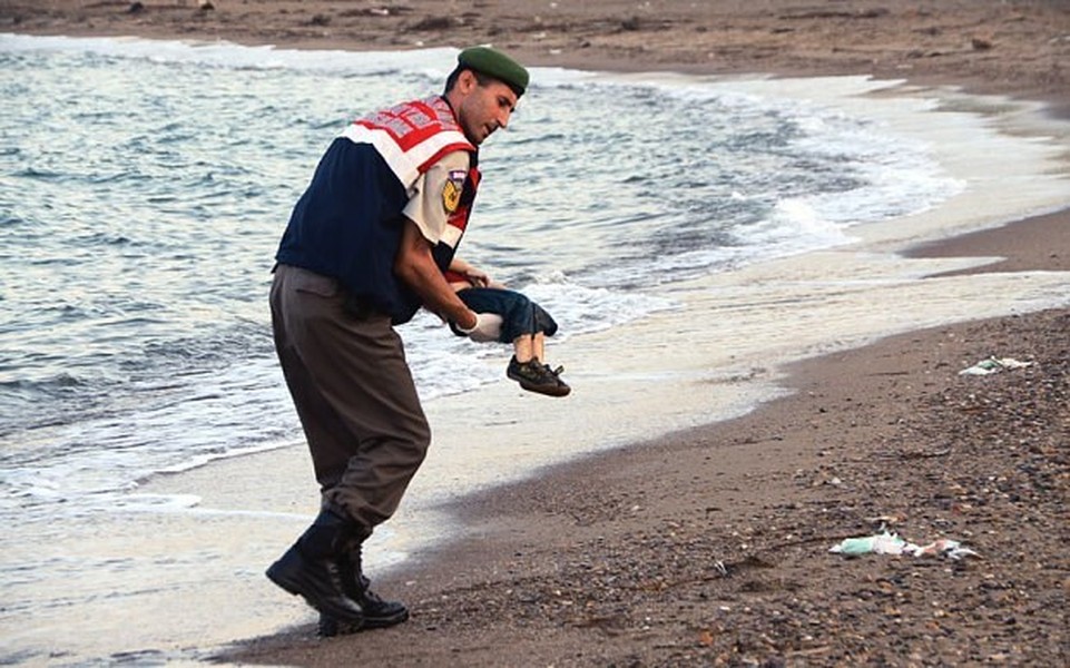 Người lính biên phòng Thổ Nhĩ Kỳ nhẹ nhàng bế thi thể bé Alan Kurdi sau khi bé dạt vào bờ biển Bodrum sau chuyến vượt biển từ đảo Kos, Hy Lạp. Đây là một trong những hình ảnh xúc động thức tỉnh lương tri về  người di cư Syria gây chấn động nhất.